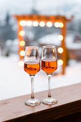 Two glasses of Aperol Spritz cocktail standing outdoors in front of romantic arc with lights.