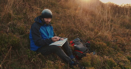 A traveler sits atop a scenic hill, carefully plotting his route with a map and compass. Serene...