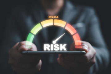 Businessman holding smartphone with risk level indicator rating since low to high for Risk management and assessment concept.