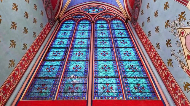 Low-angle view to the tall stained-glass window with artistic patterns inside a gothic Notre Dame cathedral, Paris, France.