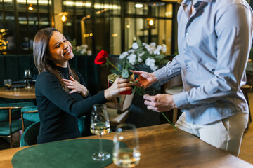 Boyfriend gifts his girlfriend beautiful red rose on a romantic dinner date.
