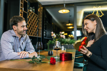 Girlfriend opens gifts from her boyfriend. They are on a romantic dinner date at the restaurant.