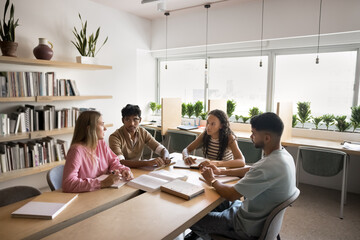 Four students sitting at table in university classroom discussing topics related to studies or joint project completion, researching, preparing for exams or admission. Team-work, knowledge exchange