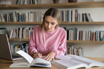Focused student girl taking notes, writing down key points from textbook, studying alone in library...