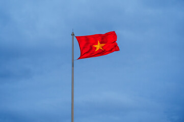 Vietnamese flag waving in the wind with clear blue sky. Yellow star on red background.
