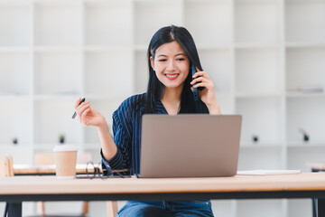 Woman working on laptop while talking on phone, multitasking in modern office.