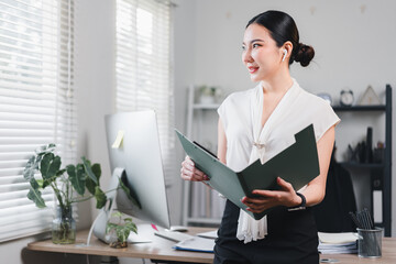 Confident asian businesswoman holding folder, standing in modern office with natural light.