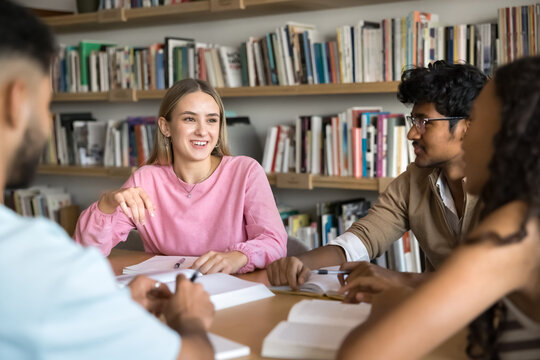 Diverse schoolmates working through assignment or math problems together in library, listening girl teammate share solutions and creative ideas, discussing key themes, engaged in educational seminar