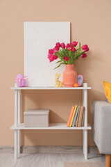 Vase with tulips, Easter eggs and painting on shelf near beige wall in room