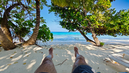 A man is laying on the beach with his feet in the sand in dhigurah maldives