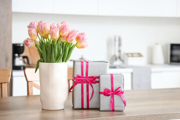 Vase with tulips and gift boxes for International Women's Day on table in kitchen
