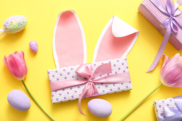 Paper bunny ears with Easter eggs, gift boxes and tulip flowers on yellow background