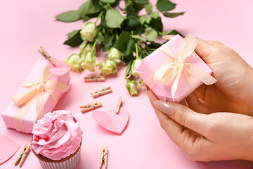 Female hands with amazing gift box and cupcake on pink background