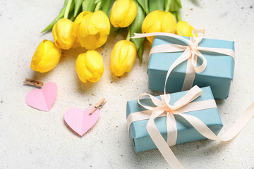 Gift boxes, fresh tulips and paper hearts on light background