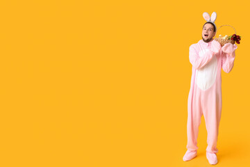 Surprised young man in bunny costume with Easter basket on yellow background