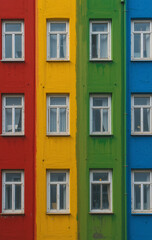 Fototapeta premium Colorful Building Façade with Symmetrical Windows, Vibrant Red, Yellow, Green, Blue Stripes, Modern Architectural Design, Urban Aesthetic Photography