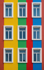 Fototapeta premium Colorful Building Façade with Symmetrical Windows, Vibrant Red, Yellow, Green, Blue Stripes, Modern Architectural Design, Urban Aesthetic Photography