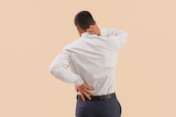 Young businessman suffering from back pain on light background