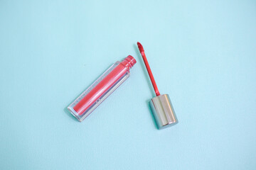 Naklejka premium Red lip gloss in elegant glass bottle with shiny lid, container with brush isolated on light blue background, red lipstick