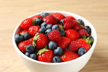 Different fresh ripe berries in bowl on wooden table