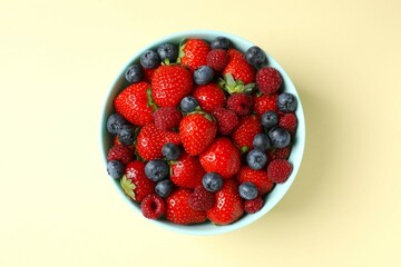 Different fresh ripe berries in bowl on color table, top view