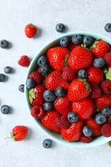 Different fresh ripe berries in bowl on gray table, top view