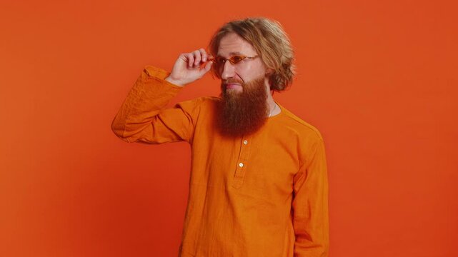 Caucasian stylish man wearing sunglasses charming smile celebrating success victory winning good positive news triumph success. People emotions concept. Redhead young guy isolated on orange background
