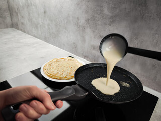 Cook pouring pancake batter into frying pan on induction cooker in prague for shrove tuesday,...