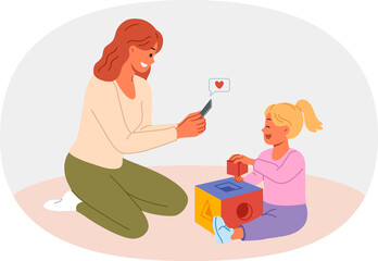 Happy mother takes photo of little daughter playing with blocks on mobile phone camera. Mother rejoices at success of pre-teen child demonstrating talent and readiness for development