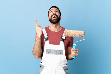 Adult painter man over isolated blue background pointing up and surprised