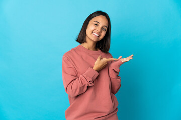 Young latin woman isolated on blue background holding copyspace imaginary on the palm to insert an...