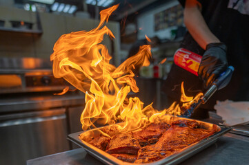 A chef skillfully uses a culinary torch to sear juicy meat, creating dramatic flames in a vibrant...