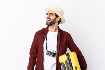 Traveler man man with beard holding a suitcase over isolated white background happy and smiling