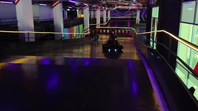 A group races gokarts at indoor track enjoying engine sounds and sharp turns