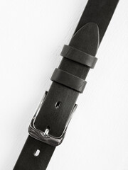 Black leather belt on a white wooden background.