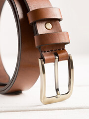 Brown leather belt on a white wooden background.