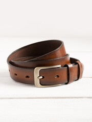 Brown leather belt on a white wooden background.