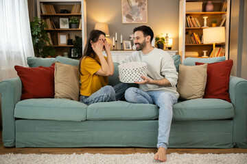 Obraz premium A thrilled woman rejoices as she reveals a thoughtful gift box, showcasing love and surprise in a charming indoor atmosphere.