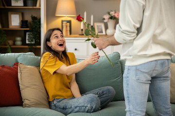 A joyful woman receives a rose, showcasing love and affection in a cozy indoor setting filled with...