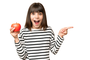 Little girl with an apple over isolated chroma key background surprised and pointing finger to the...