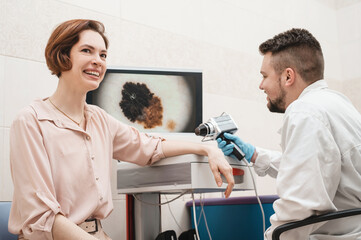 Male doctor examines neoplasms or moles on the woman patient's skin - using special apparatus for...
