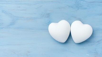 Obraz premium Two white decorative hearts placed side by side on a rustic blue wooden background.
