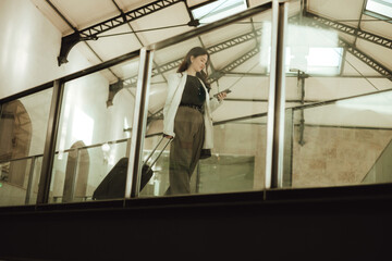 Vlogger traveler woman with suitcase using phone at train station in Lisbon. Business travel and solo tourism concept. Gen Z girl influencer shooting social media stories on the street