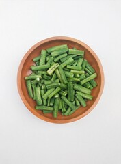 Long beans (Vigna Unguiculata ssp. Sesquipedalis) that have been cut into pieces in a wooden bowl on a white background. Top of view. 