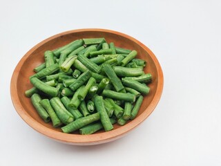 Long beans (Vigna Unguiculata ssp. Sesquipedalis) that have been cut into pieces in a wooden plate on a white background.