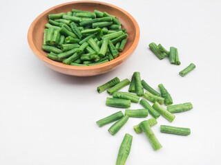 High angle view of long beans (Vigna Unguiculata ssp. Sesquipedalis) that have been cut into pieces in a wooden bowl on a white background.