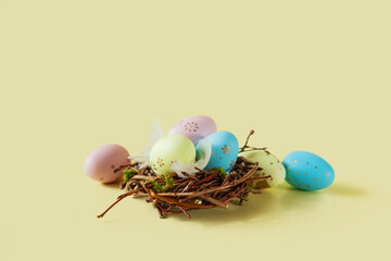 Painted eggs and feathers in a nest on a light yellow background.