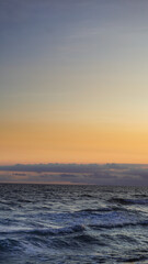 Serene ocean waves at sunset with a golden sky and soft clouds. A tranquil seascape perfect for travel, nature, and relaxation themes.