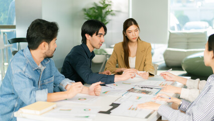 A group of young professionals engaged in a collaborative discussion around a table, analyzing documents and brainstorming ideas in a modern office environment. © Leny Studio