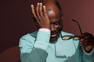 Elderly Man Holding Glasses with Hand on Forehead